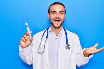 Young handsome man wearing doctor stethoscope holding syringe celebrating achievement with happy smile and winner expression with raised hand