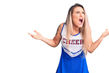 Young beautiful blonde woman wearing cheerleader uniform crazy and mad shouting and yelling with...