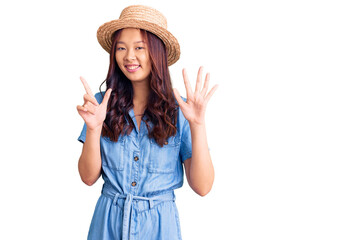 Obraz na płótnie Canvas Young beautiful chinese girl wearing summer hat showing and pointing up with fingers number seven while smiling confident and happy.