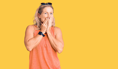 Middle age fit blonde woman wearing casual summer clothes and sunglasses laughing and embarrassed giggle covering mouth with hands, gossip and scandal concept