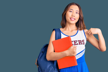 Young beautiful chinese girl wearing cheerleader uniform and student backpack holding binder...