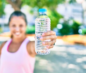 Middle age sportswoman smiling happy holding bottle of water at the park