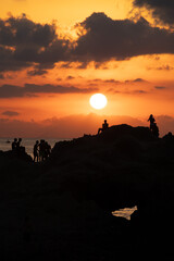 Sunset silhouettes. Groups of young people looking at the sunset from a rock in the sea on the coast of Tropea, Calabria. italian summer and vacation mood, amazing colored sunset sky, reflections.