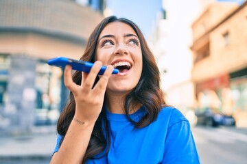 Young hispanic woman smiling happy sending voice message using smartphone at the city.