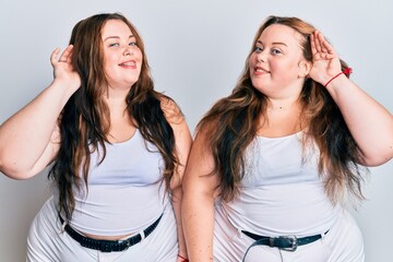 Plus size caucasian sisters woman wearing casual white clothes smiling with hand over ear listening an hearing to rumor or gossip. deafness concept.