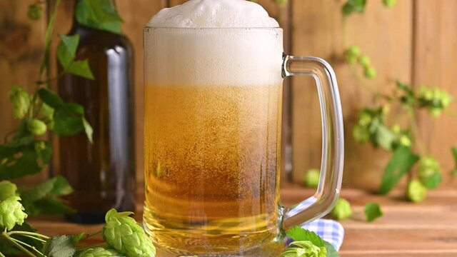 Beer. Cold Craft light Beer in a glass with water drops. Pint of Beer close up on a wooden background. Beer is pouring from the bottle. Border design. High quality 4k footage