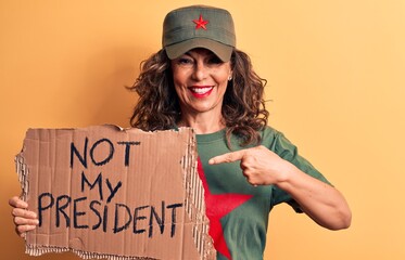 Middle age brunette communist woman holding banner with not my president message smiling happy pointing with hand and finger
