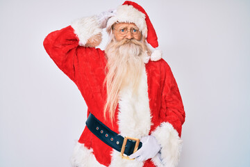 Old senior man with grey hair and long beard wearing santa claus costume with suspenders confuse and wonder about question. uncertain with doubt, thinking with hand on head. pensive concept.