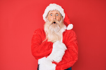 Old senior man with grey hair and long beard wearing traditional santa claus costume afraid and shocked with surprise expression, fear and excited face.