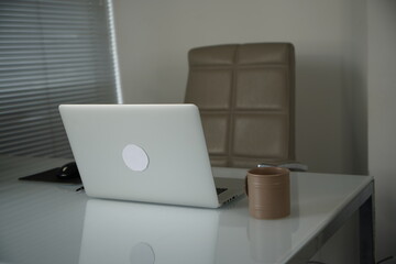 Close up view of simple workspace with laptop, smartphone, coffee cup and tree pot on white table with blurred office room background.