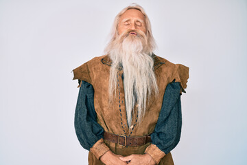 Old senior man with grey hair and long beard wearing viking traditional costume looking at the camera blowing a kiss on air being lovely and sexy. love expression.
