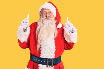 Old senior man with grey hair and long beard wearing traditional santa claus costume gesturing finger crossed smiling with hope and eyes closed. luck and superstitious concept.