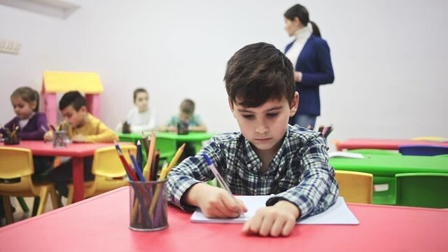 Portrait of little assiduous boy with pen and notebook at lesson in elementary school