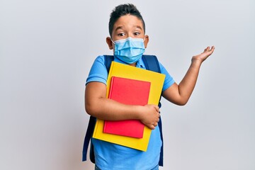 Little boy hispanic kid wearing medical mask going to school celebrating achievement with happy smile and winner expression with raised hand