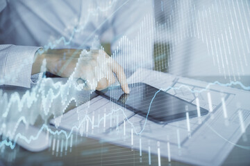 Double exposure of man's hands holding and using a digital device and forex graph drawing. Financial market concept.