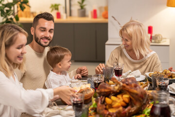 Happy mature blond female looking at her grandson sitting on knees of his father