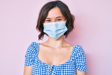 Young beautiful woman wearing medical mask looking positive and happy standing and smiling with a confident smile showing teeth