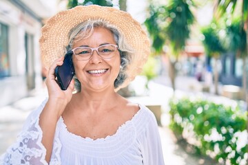 Middle age woman with grey hair smiling happy outdoors speaking on the phone