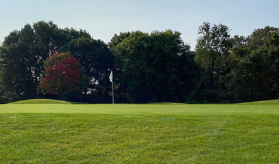 Fototapeta na wymiar golf course red leaves late summer early autumn green white flag 