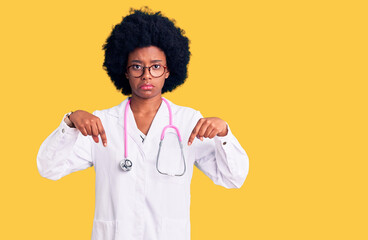 Young african american woman wearing doctor coat and stethoscope pointing down looking sad and upset, indicating direction with fingers, unhappy and depressed.