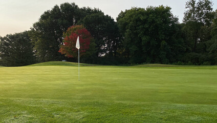 Obraz premium late summer early autumn golf course green red leaves on tree white flag 