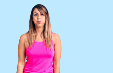 Young beautiful woman wearing sportswear puffing cheeks with funny face. mouth inflated with air,...