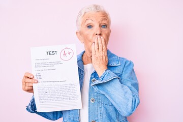 Senior beautiful woman with blue eyes and grey hair showing a passed exam covering mouth with hand, shocked and afraid for mistake. surprised expression