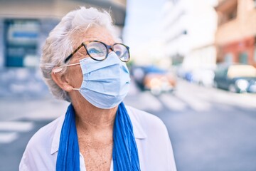 Elder senior woman with grey hair wearing coronavirus safety mask outdoors