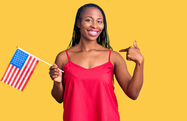 Young african american woman holding united states flag pointing finger to one self smiling happy and proud