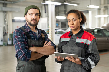 Two young serious workers of car maintenance center in uniform working in hangar