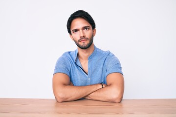 Handsome hispanic man wearing casual clothes sitting on the table skeptic and nervous, disapproving...