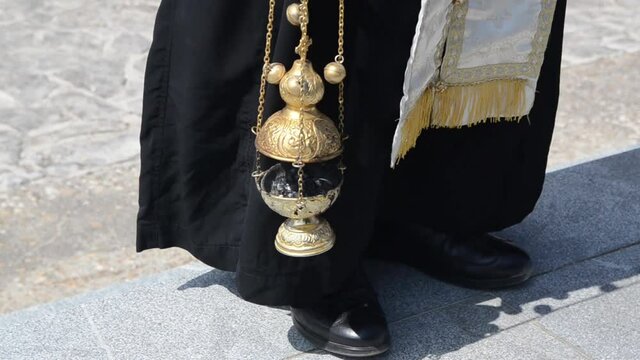 A priest swings a thurible on missal. Orthodox priest with hand censer during worship service. Censer used during liturgy. Man swinging chain censer. 