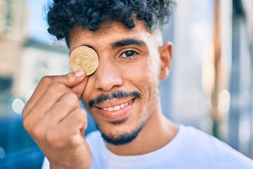 Young arab man smiling happy holding golden bitcoin walking at street of city.