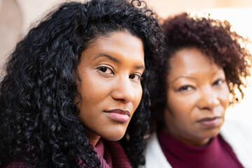 Profile of brazilian adult daughter and mother with serious expression looking at camera outside...
