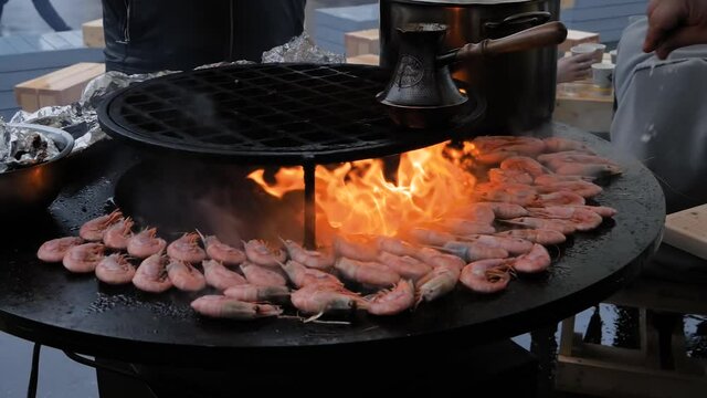 Super slow motion: chef grilling fresh red king prawns on brazier with hot flame at summer local food market - close up. Outdoor cooking, barbecue, gastronomy, seafood, cookery, street food concept