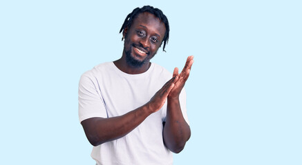 Young african american man with braids wearing casual white tshirt clapping and applauding happy and joyful, smiling proud hands together