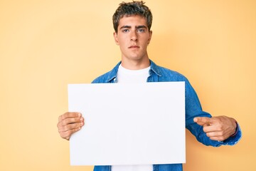 Young handsome man holding blank empty banner relaxed with serious expression on face. simple and...