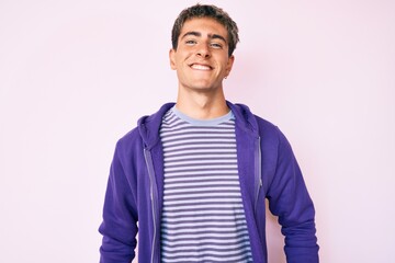 Young handsome man wearing casual purple sweatshirt looking positive and happy standing and smiling with a confident smile showing teeth