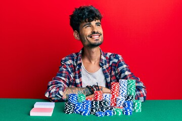 Young hispanic man sitting on the table with poker chips and cards looking to side, relax profile...
