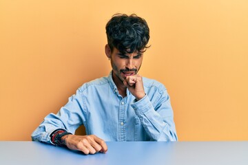 Young hispanic man wearing casual clothes sitting on the table feeling unwell and coughing as...