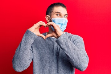 Young handsome man wearing medical mask smiling in love doing heart symbol shape with hands. romantic concept.