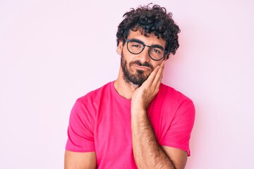 Fototapeta na wymiar Handsome young man with curly hair and bear wearing casual clothes and glasses thinking looking tired and bored with depression problems with crossed arms.