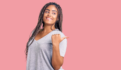 Young african american woman with braids wearing casual clothes smiling with happy face looking and pointing to the side with thumb up.