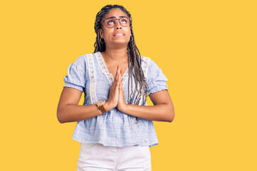 Young african american woman with braids wearing casual summer clothes and glasses begging and praying with hands together with hope expression on face very emotional and worried. begging.