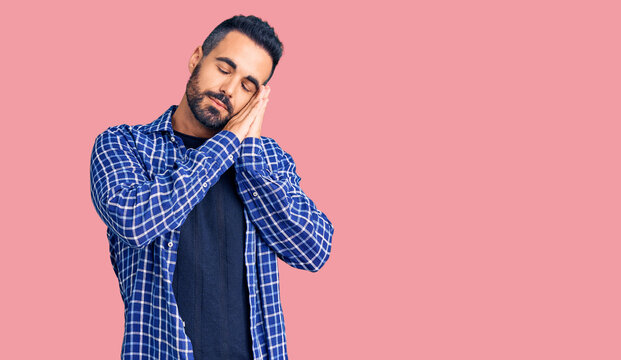 Young hispanic man wearing casual clothes sleeping tired dreaming and posing with hands together while smiling with closed eyes.