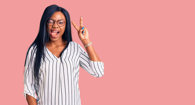 Young african american woman wearing casual clothes and glasses smiling with happy face winking at the camera doing victory sign with fingers. number two.
