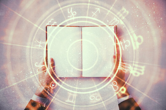 Close up of hands holding abstract book with zodiac wheel.