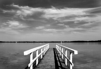 Fototapeta na wymiar lonely wooden bridge at a calm lake with a cloudy sky in black and white