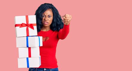 Beautiful african american woman holding presents annoyed and frustrated shouting with anger, yelling crazy with anger and hand raised