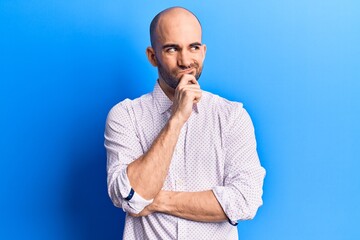 Young handsome bald man wearing elegant shirt thinking concentrated about doubt with finger on chin and looking up wondering